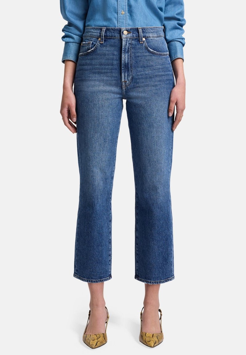 Jean en denim bleu taille haute avec une coupe droite, présentant un délavage, un design à cinq poches et des détails de couture minimalistes.