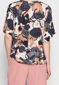 Blusa floreale multicolore con taglio ampio, maniche corte e tessuto morbido con un design giocoso, abbinata a pantaloni rosa.