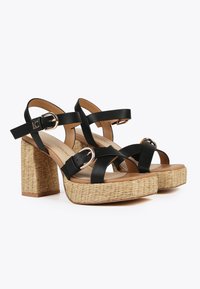 Sandalias de tacón alto negras con tiras, plataforma trenzada y tacón cuadrado. Cuentan con hebillas ajustables y una textura suave similar al cuero.