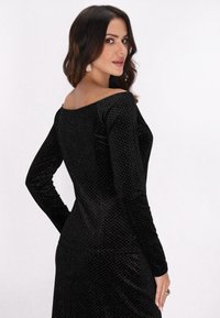 Fekete bársony, hosszú ujjú ruha, off-shoulder nyakkivágással, finom gyémántmintázattal és testhez simuló fazonnal.