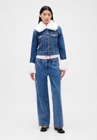 Denimjack met nepbontkraag en manchetten, pastelkleurige geribbelde tailleband, en wijde denimbroek. De outfit heeft een blauw kleurenschema.