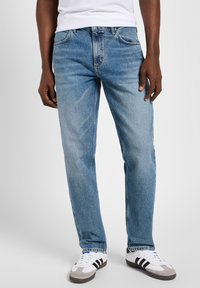 Jeans de mezclilla azul claro con corte recto, que presentan un diseño clásico de cinco bolsillos y un ligero desvanecimiento. Combinados con zapatillas blancas y grises.