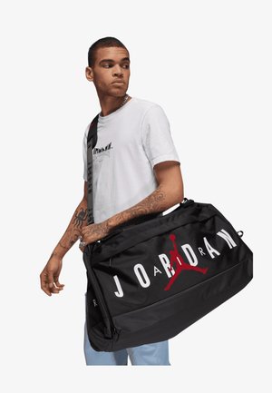 Borsa a tracolla nera con il marchio "JORDAN" in bianco e rosso, caratterizzata da un logo Jumpman rosso, tessuto resistente e chiusura superiore con zip.