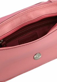 Bolso de piel rosa con un acabado texturizado, con un bolsillo con cremallera y un cierre a presión. Interior forrado en una tela de rosa más oscuro, mostrando la etiqueta de la marca.