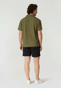 Olivgrön kortärmad polo skjorta kombinerad med svarta shorts och vita sneakers. Skjortan har en standardkrage och en avslappnad passform.
