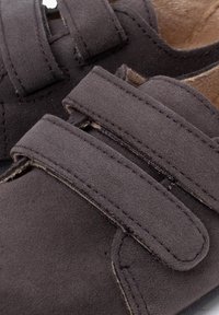 Scarpe scure in suede grigio con due cinturini regolabili in Velcro, design arrotondato e finitura testurizzata. L'interno presenta una fodera marrone chiaro.