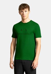 Zeleni kratkosleeven majica iz mehkega materiala z okroglim ovratnikom in črnim natisnjenim logotipom "A/X ARMANI EXCHANGE" spredaj.