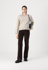 Bežinė megztinė tiesaus silueto, derinama su rudomis švelniomis kelnėmis ir juodais bateliais. Maža juoda petnešėlių kuprinė kaip akcentas.