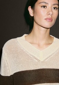 Maglione lavorato a maglia con scollo a V, caratterizzato da strisce orizzontali alternate in crema e marrone scuro, realizzato in un tessuto leggero e testurizzato.
