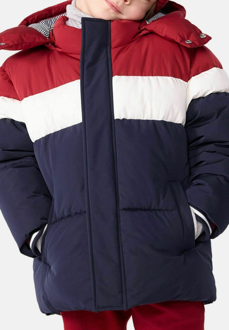 Veste d'hiver rembourrée présentant des rayures horizontales rouges, blanches et bleu marine, un col haut et des poches latérales. Texture de tissu lisse et isolé.