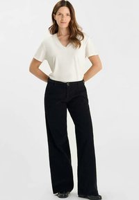 Maglietta bianca a scollo a V abbinata a pantaloni neri a gamba larga. La maglietta è aderente, mentre i pantaloni sono realizzati in un materiale strutturato con una finitura liscia.