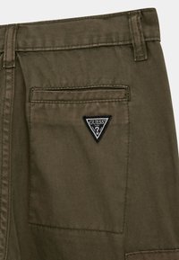 Olivgröna cargobyxor med bakficka som har en svart, triangel-formad patch med Guess-logotyp samt fina diagonala sömmar.