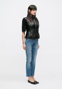 Čierna prešívaná vesta s vysokým golierom, krátkymi rukávmi a zapínaním na zips, kombinovaná so svetlomodrými rifle s rovnými nohavicami a čiernymi balerínkami.