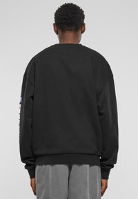 Czarny, oversize sweatshirt z okrągłym dekoltem, z kolorowym wzorem graficznym na lewym rękawie, wykonany z miękkiego, teksturowanego materiału.