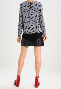 Maglietta a maniche lunghe con un motivo geometrico blu navy e grigio, con apertura a chiave sulla schiena. Abbinata a una gonna nera effetto pelle e sandali con tacco rossi.