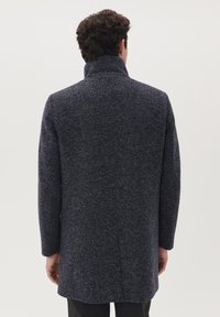 Cappotto di lana navy con finitura strutturata, colletto alto e maniche lunghe, caratterizzato da un taglio dritto e senza chiusure visibili sul retro.