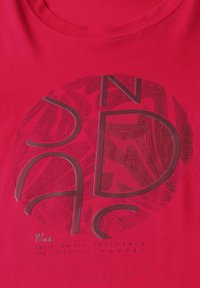 T-shirt en coton rouge avec un graphisme texturé et un texte superposé en noir et argent contrasté, délimitant un design circulaire.