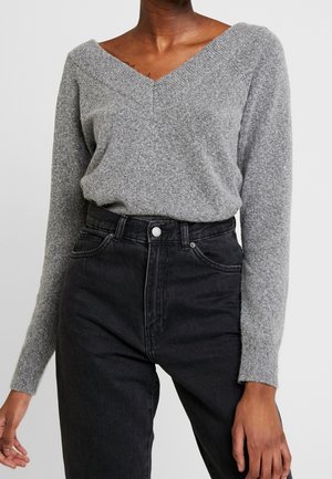Grijze gebreide trui met een V-hals en lange mouwen, gecombineerd met zwarte denim jeans met hoge taille. De textuur lijkt zacht en iets losvallend.