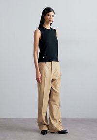 Un haut noir sans manches associé à un pantalon large beige. Le haut a un col rond, et le pantalon est coupé avec une coupe décontractée.