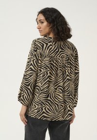 Blouse à motif zèbre marron et noir avec un dos froncé, des manches longues et une coupe décontractée, fabriquée à partir d'un tissu léger.