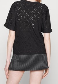 Černá halenka s dírkovaným vzorem a krátkými nabíranými rukávy. Spárována s černou minisukní se pruhy.