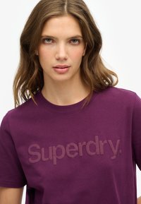 Fioletowa bawełniana koszulka z subtelnym wytłoczonym logo "Superdry" na klatce piersiowej oraz klasycznym okrągłym dekoltem.