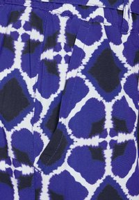 Tessuto viola con un motivo astratto audace in blu scuro e bianco. Include pieghe e dettagli di cucitura visibili.