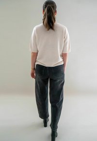 Haut en tricot blanc à manches courtes, associé à un jean en denim noir à taille haute et coupe ample. Des bottines noires à la cheville complètent la tenue.