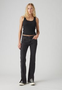 Black tank top paired with dark denim flared jeans. The jeans feature a textured seam detail and are styled with black and white sneakers.