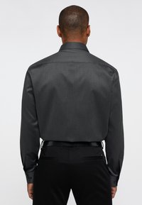 Donkergrijs overhemd met een subtiele textuur, lange mouwen en een puntige kraag. Zwarte broek met een strakke pasvorm en zonder zichtbare patronen.