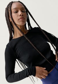 Top negro de manga larga acanalada con cuello redondo y diseño ajustado. La tela texturizada presenta puños de manga extendidos.