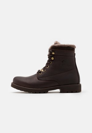 Bottine en cuir brun foncé avec doublure en fourrure, œillets dorés, semelle robuste et logo en relief sur le côté, vue du côté extérieur.