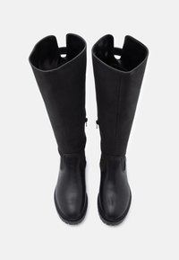 Botas de rodilla negras con una mezcla de cuero liso y ante. Presentan una puntera redondeada, paneles laterales elásticos y una lengüeta en la parte superior.