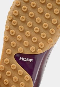 Semelle de chaussure en caoutchouc beige texturé avec des motifs circulaires antidérapants et un accent bordeaux. Le mot « HOFF » est embossé en blanc.