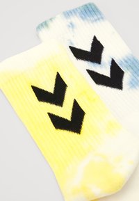 Färgglada ankelsockor med ett tie-dye-mönster i gult och blått, med svart chevron-design på kontrasterande bakgrunder. Ribbad textur.