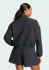 Fekete bomberdzseki magas gallérral, rugalmas mandzsettákkal és derékpánttal. Simított textúra, laza szabás, fekete rövidnadrággal párosítva.