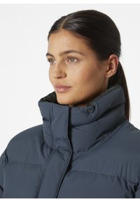 Námorně modrá puffa bunda s vysokým límcem, která má knoflíkové zapínání a texturovanou tkaninu. Hladký povrch s izolací pro teplo.