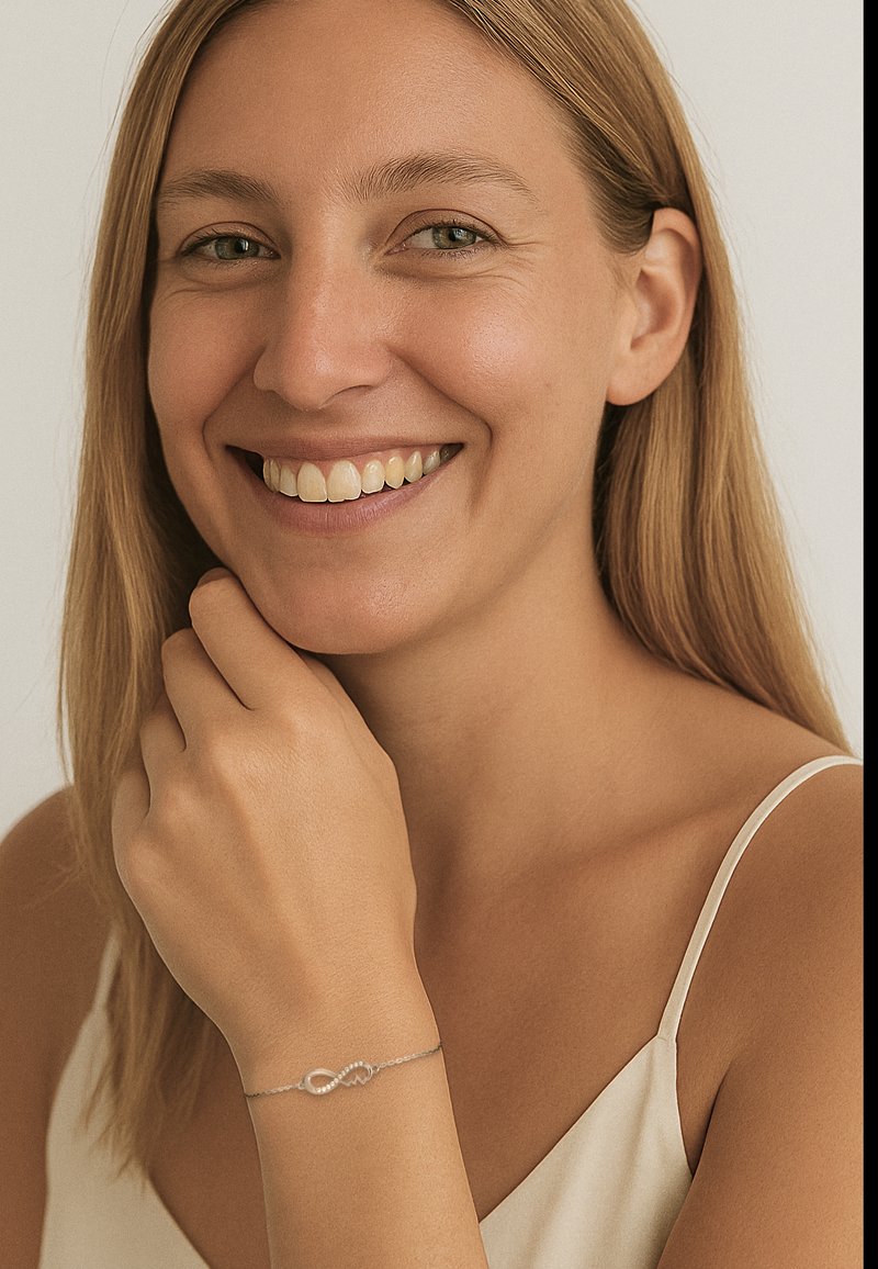 Braccialetto infinito in argento indossato su una mano dalla superficie liscia; presenta una delicata catena e un simbolo dell'infinito lucidato. Il tono della pelle è chiaro.