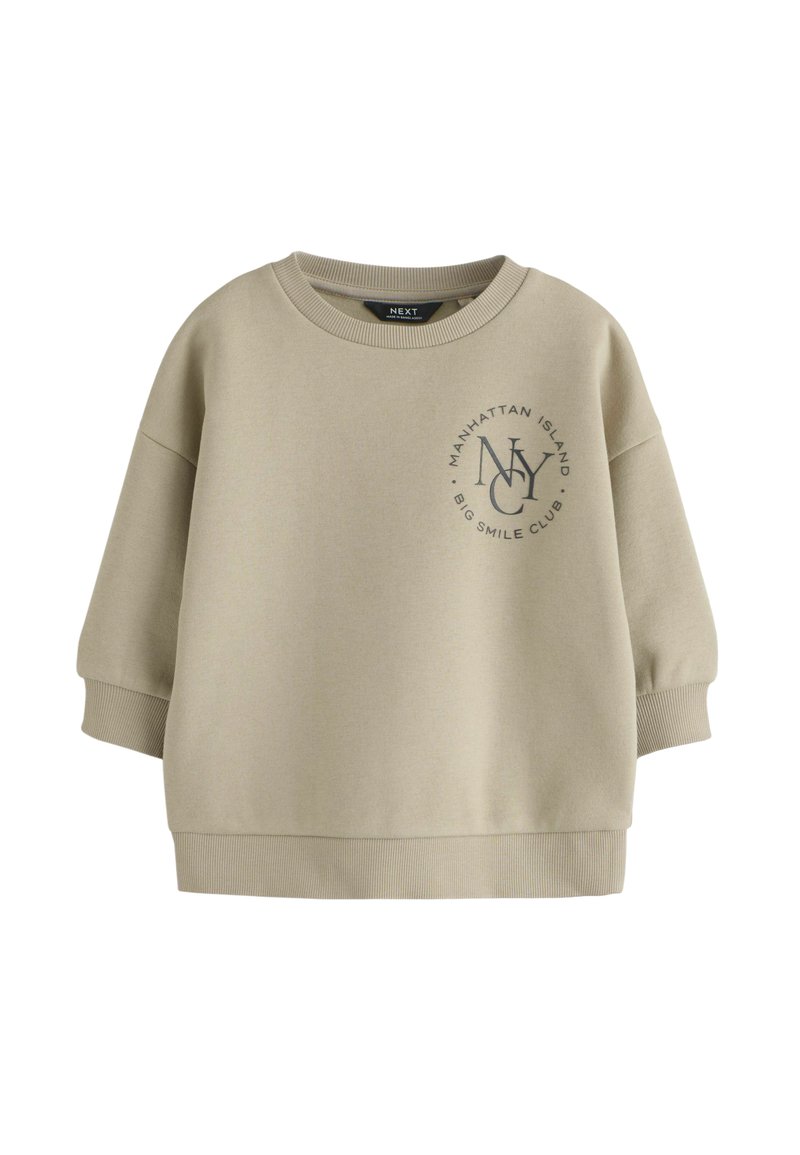 Felpa beige chiaro realizzata in misto cotone. Presenta un collo rotondo, spalle scese e una stampa con "NY" e testo sulla parte anteriore.