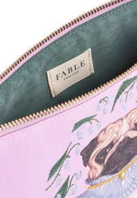 Rozā kosmētikas soma ar pugu ilustrāciju un ziedu akcentiem, mīksts audums, zaļa oderējuma krāsa un zelta tonis rāvējslēdzēju aparatūrā. Redzama FABLE etiķete.