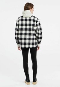 Gequilted zwart-wit geruite jas met een lichtgekleurde capuchon, gecombineerd met zwarte legging en chunky zwarte laarzen.