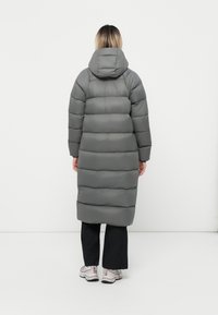Lange, gevoerde grijze jas met een capuchon, met een gewatteerd ontwerp en een rechte snit. G gedragen met zwarte broek en lichte sneakers.