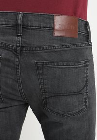 Svarta denimjeans med en åtsittande form, med två bakfickor och en brun läderlapp med "Hollister"-logotypen vid midjan.