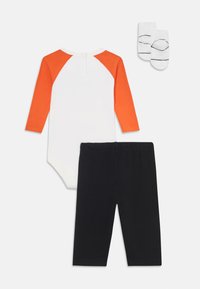 Three-piece outfit includes a white bodysuit with orange raglan sleeves, black pants, and white socks with black stripes.