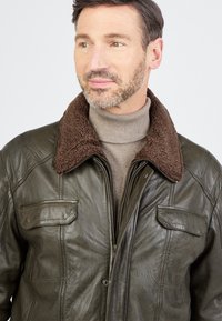 Braune Lederjacke mit einem braunen Schafslederkragen, frontseitigem Reißverschluss und zwei Brusttaschen, gestaltet mit einer glatten Textur und maßgeschneidertem Schnitt.