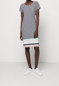 Sukienka w paski w kolorze granatowym i białym, z wielokolorowym paskiem u dołu w kolorach miętowym, różowym i granatowym, oraz małą kieszonką na piersi.