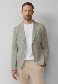 Jasnoszary blazer o teksturowanej powierzchni wykonany z tkaniny w tkanym wzorze, z dwoma guzikami, pojedynczą kieszenią na piersi, w połączeniu z białą koszulą i beżowymi spodniami.