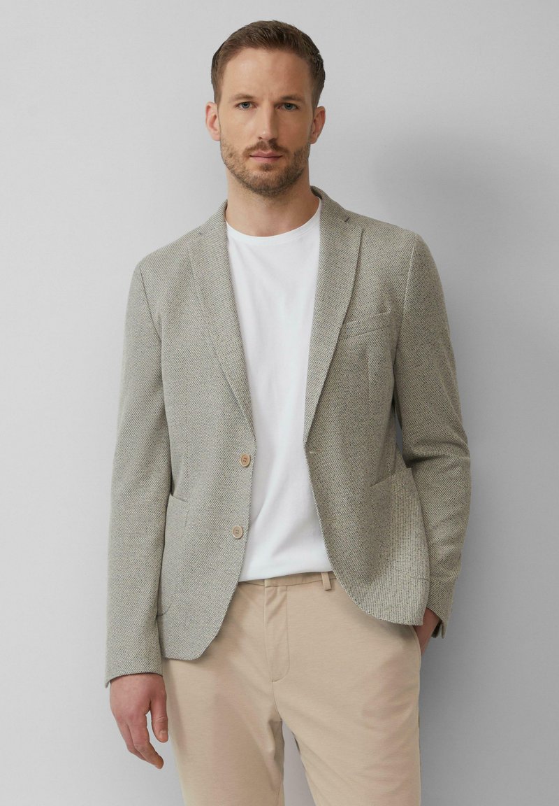Jasnoszary blazer o teksturowanej powierzchni wykonany z tkaniny w tkanym wzorze, z dwoma guzikami, pojedynczą kieszenią na piersi, w połączeniu z białą koszulą i beżowymi spodniami.