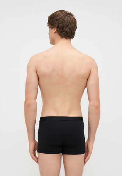 Boxers de algodão pretos com uma faixa elástica suave, exibidos em um modelo visto de costas sobre um fundo claro e liso.