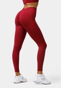 High-waisted red leggings featuring a ribbed texture and contouring design, paired with white athletic shoes.